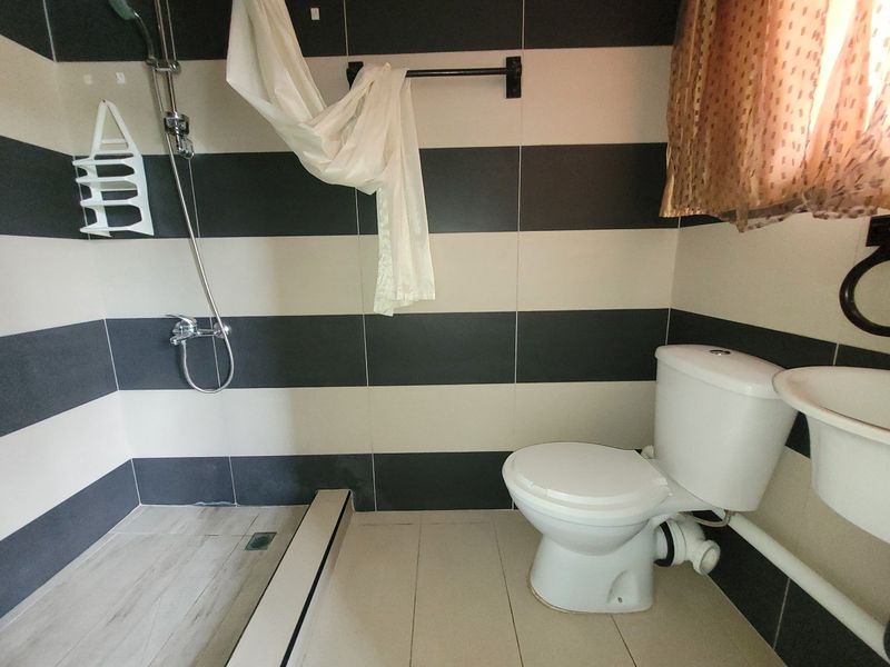 A compact bathroom featuring black and white horizontal wall tiles, a standard toilet, wall-mounted basin, and a shower area with exposed plumbing.