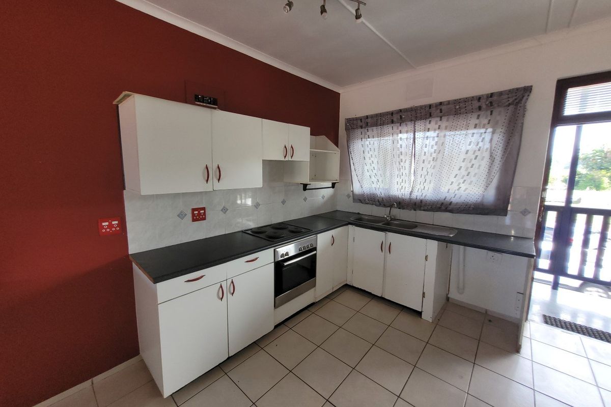 A functional kitchen featuring white cabinetry, dark laminate countertops, a built-in oven and hob, and tiled flooring with direct access to an outdoor area.