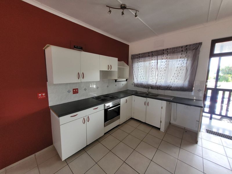 A functional kitchen featuring white cabinetry, dark laminate countertops, a built-in oven and hob, and tiled flooring with direct access to an outdoor area.