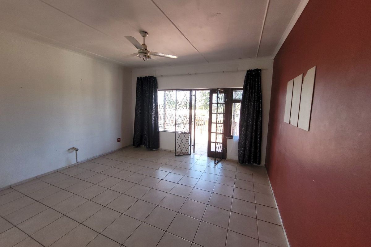 Spacious living area featuring neutral tiled flooring, a ceiling fan, and direct access to an outdoor space through a secure glass door.