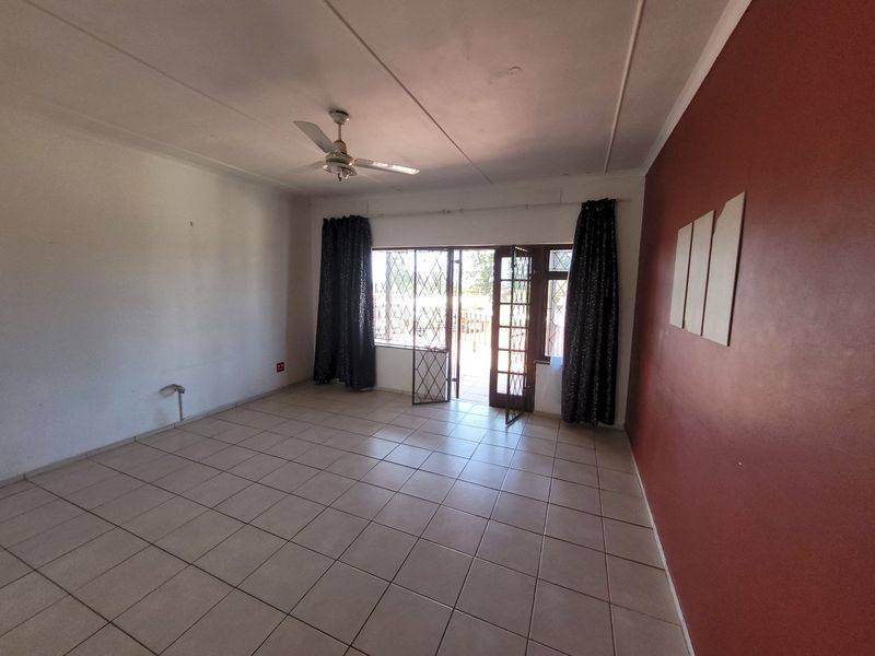 Spacious living area featuring neutral tiled flooring, a ceiling fan, and direct access to an outdoor space through a secure glass door.
