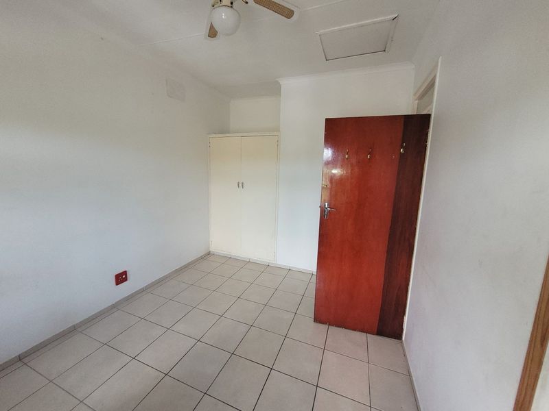 An empty bedroom featuring tiled flooring, a built-in cupboard, and a ceiling fan, offering a blank canvas for personalization.