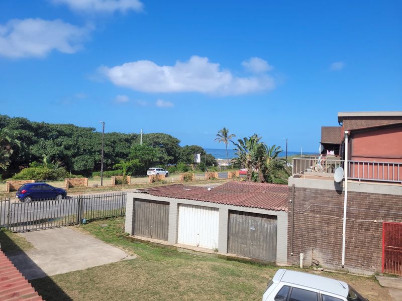 Elevated view overlooking the property grounds, featuring a multi-bay garage structure, brick exterior, and distant ocean views.