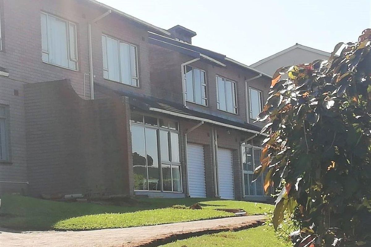 Rear view of a multi-story apartment complex featuring brick exterior, aluminium windows, sliding glass doors, and integrated garage access with a paved walkway.