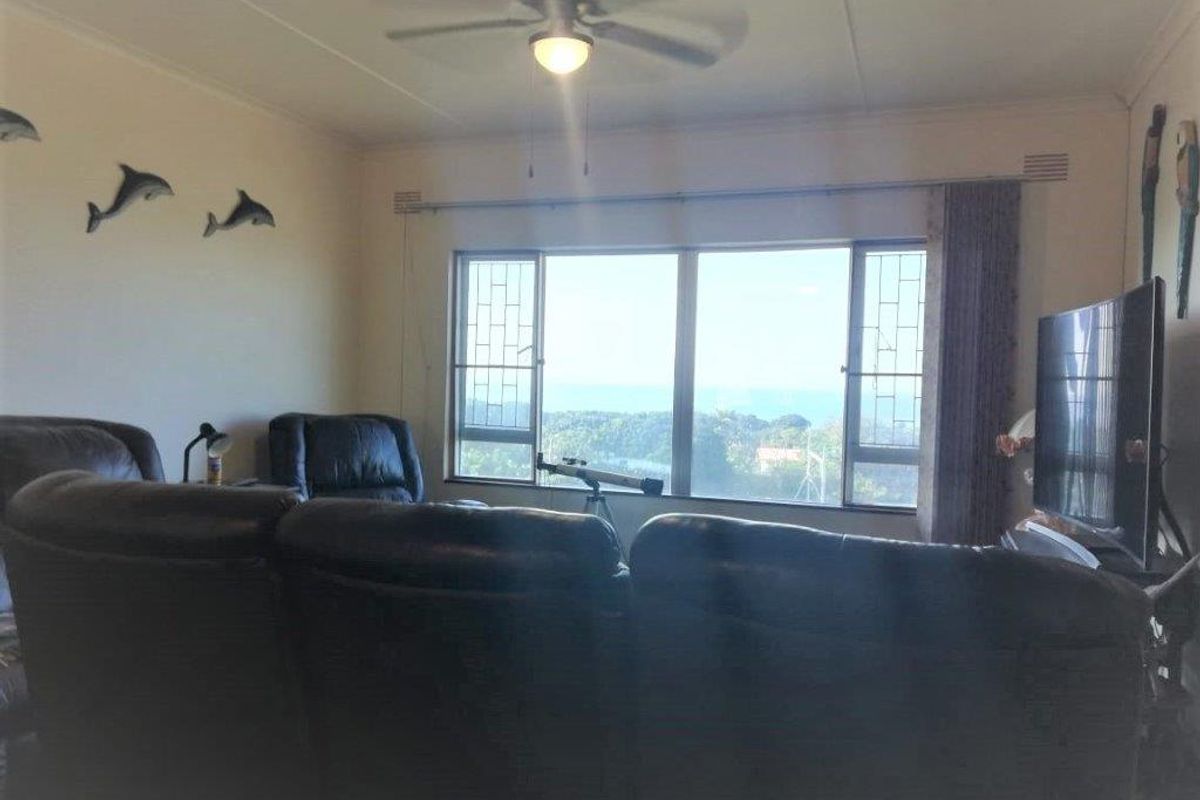 A living room featuring a ceiling fan and a large window with security bars, offering a view of the surrounding area.