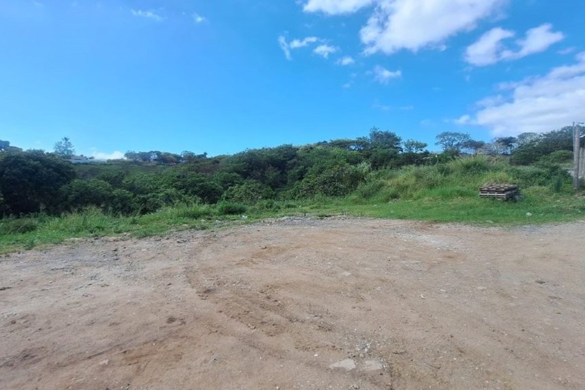 A view of a vacant residential plot featuring an unpaved access area, natural vegetation, and surrounding landscape.