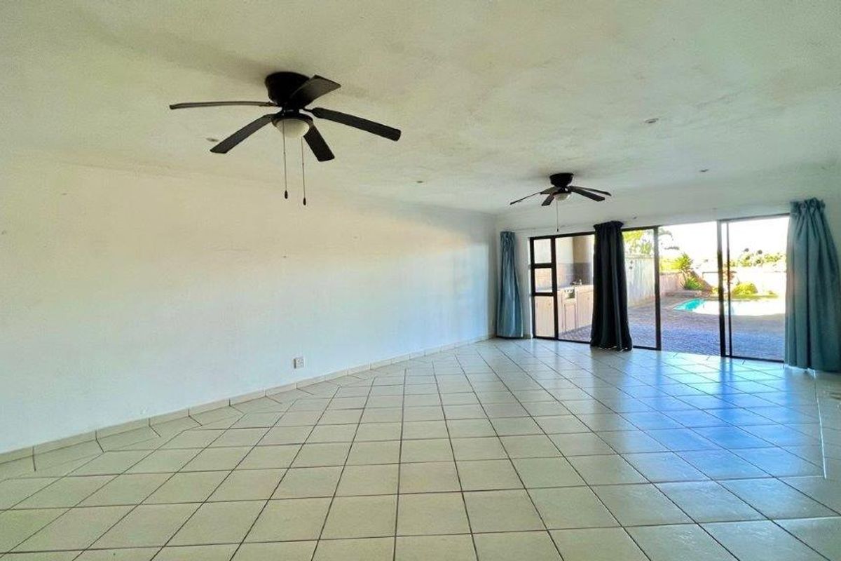 Spacious, empty living area featuring tiled flooring, dual ceiling fans, and large sliding glass doors providing direct access to the outdoor pool area.