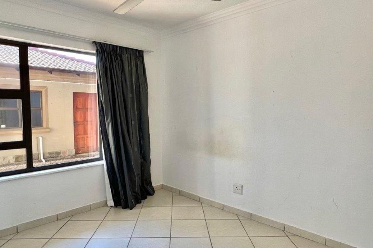 An empty bedroom featuring tiled flooring, a ceiling fan, and large aluminium-framed windows, requiring minor cosmetic updates to the walls.