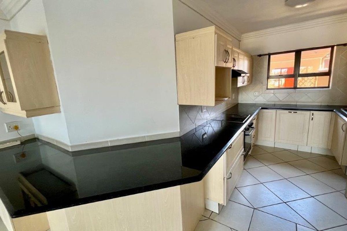 A functional kitchen featuring light wood cabinetry, contrasting black granite countertops, built-in oven and hob, and tiled flooring throughout.