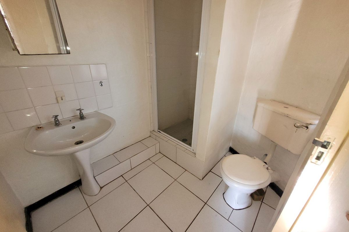 A dated bathroom featuring a pedestal basin, shower enclosure, and toilet with white tiled flooring and splashbacks, requiring cosmetic updates.