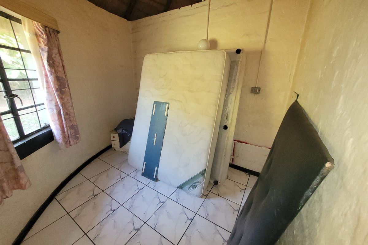 A small bedroom featuring tiled flooring and an exposed thatch ceiling, currently vacant and in need of cosmetic refurbishment.