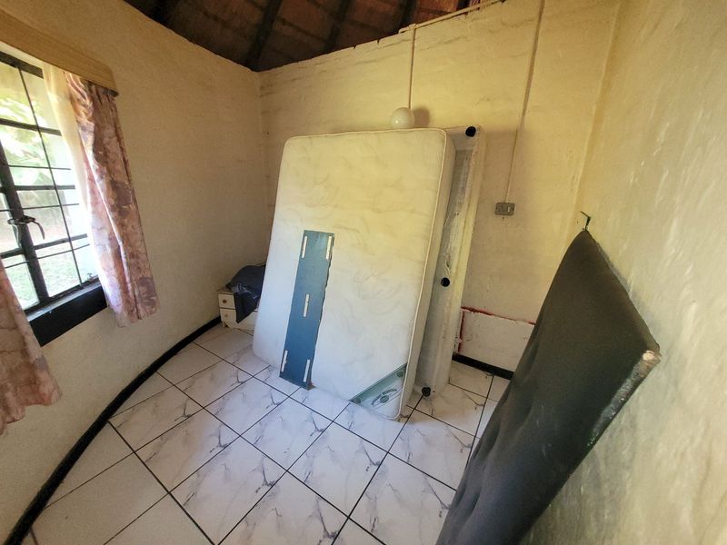 A small bedroom featuring tiled flooring and an exposed thatch ceiling, currently vacant and in need of cosmetic refurbishment.