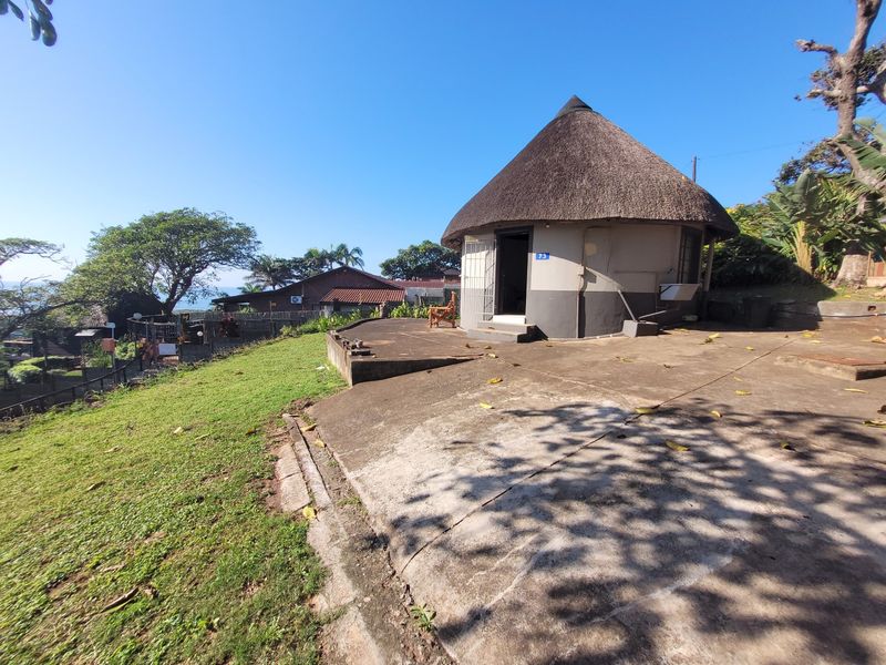 Exterior view of a circular townhouse unit featuring a traditional thatch roof and an expansive concrete patio area set within a garden.