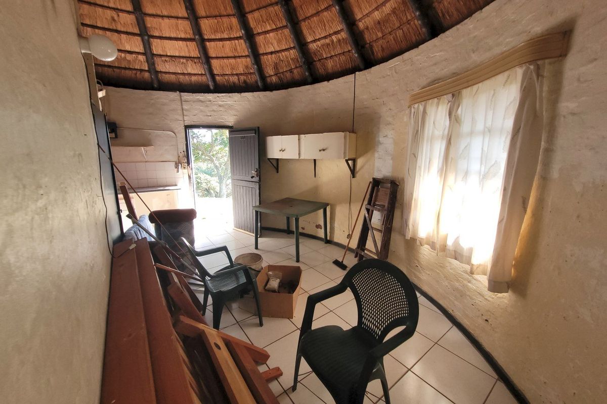 A circular living space featuring a traditional thatched roof with exposed rafters, tiled flooring, and built-in wall cabinetry, requiring cosmetic updates.