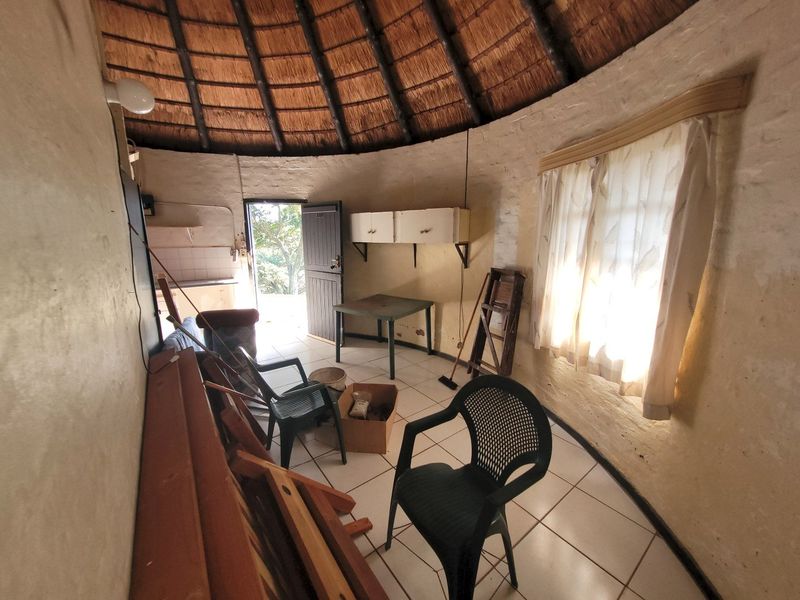 A circular living space featuring a traditional thatched roof with exposed rafters, tiled flooring, and built-in wall cabinetry, requiring cosmetic updates.