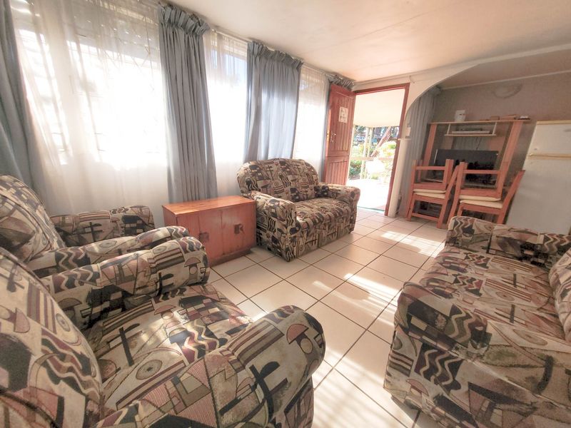A living room featuring tiled flooring and large windows, providing direct access to an outdoor area.