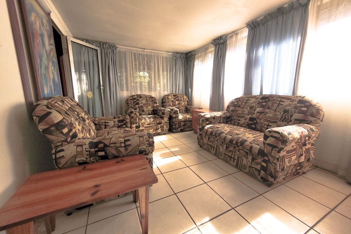 A sunlit living room featuring ceramic floor tiles and large windows, offering a bright and functional space for relaxation.