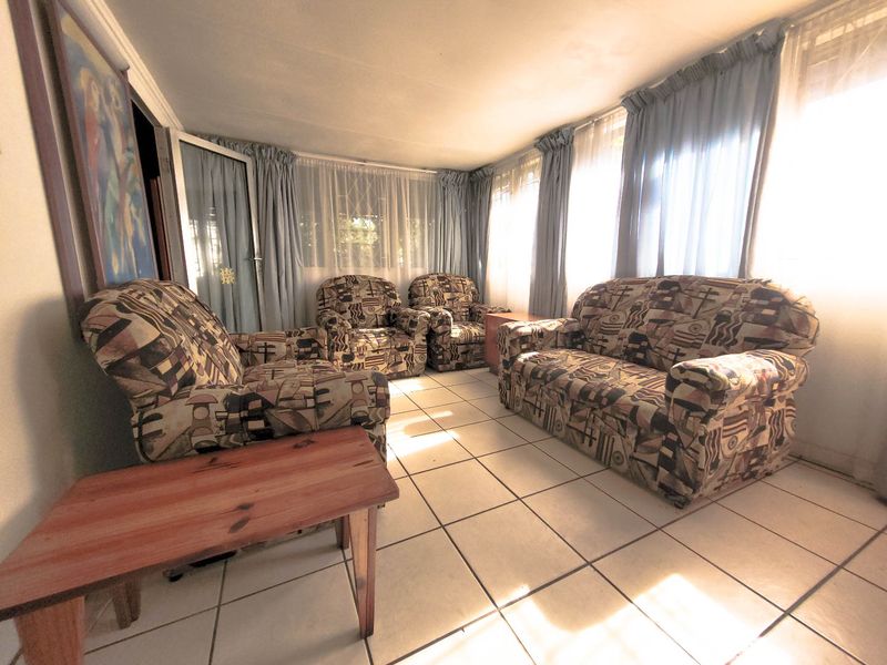 A sunlit living room featuring ceramic floor tiles and large windows, offering a bright and functional space for relaxation.