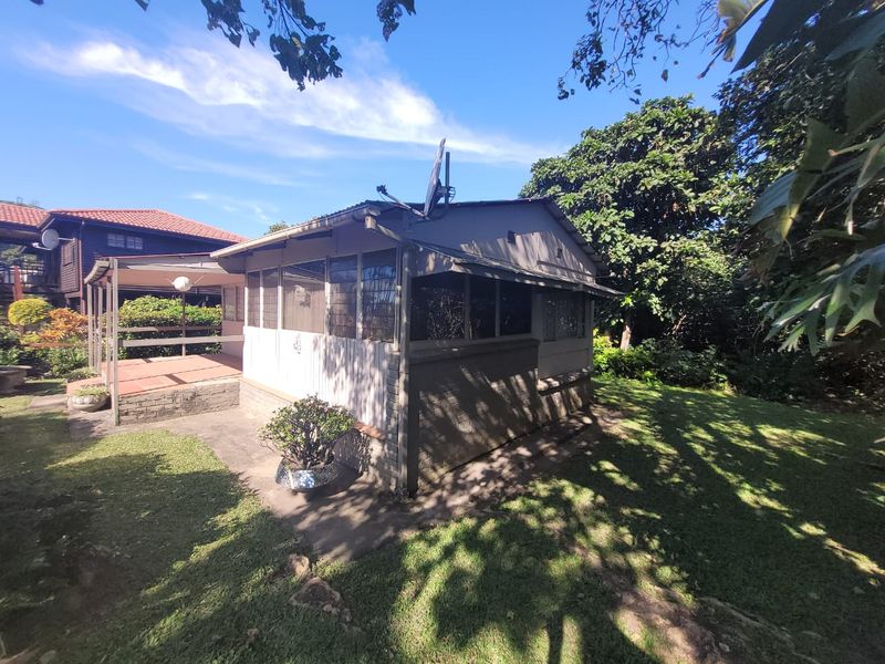 Rear view of the townhouse featuring a covered tiled patio, brick foundation, and established garden surroundings.
