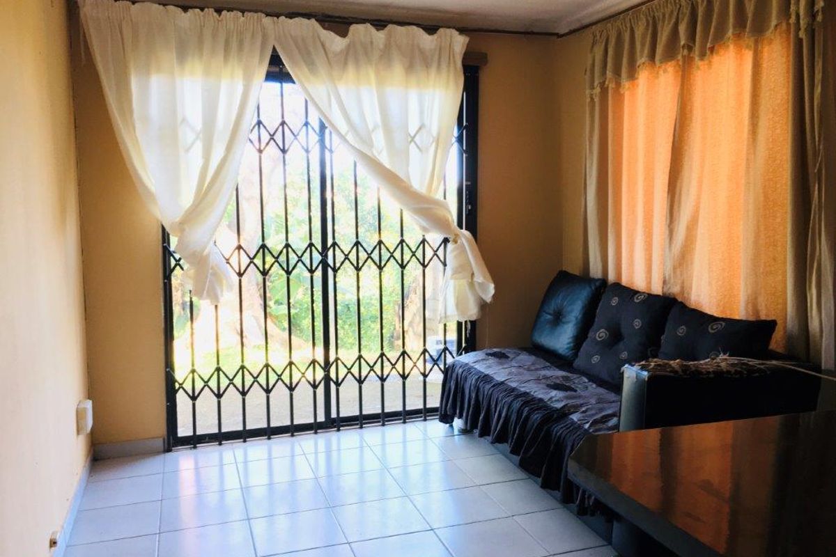 A living room featuring tiled flooring and a sliding glass door secured with a metal security gate, providing access to the exterior.