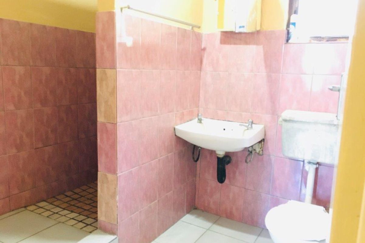 A functional bathroom featuring pink wall tiles, a wall-mounted basin, and a standard toilet with a separate shower area.