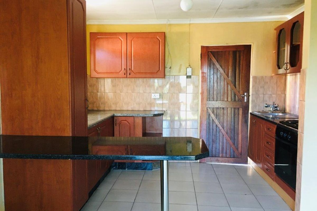 A dated kitchen featuring wooden cabinetry, tiled splashbacks, a breakfast bar, and a built-in oven with a hob.