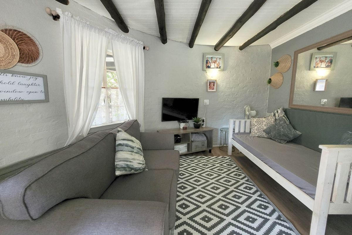 A cozy living room featuring exposed timber ceiling beams, painted brick walls, and durable laminate flooring, creating a rustic and inviting atmosphere.