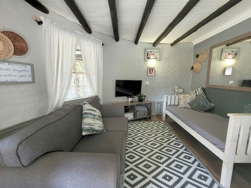 A cozy living room featuring exposed timber ceiling beams, painted brick walls, and durable laminate flooring, creating a rustic and inviting atmosphere.