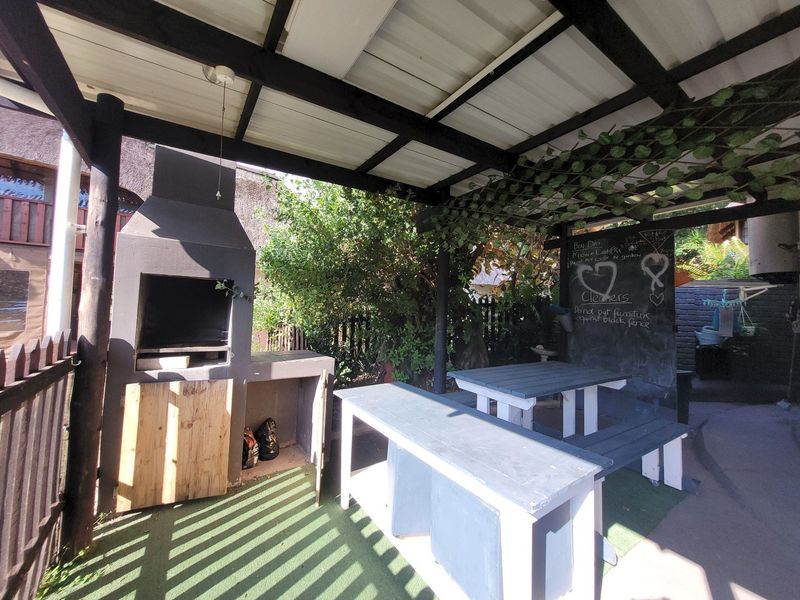 Covered outdoor patio area featuring a built-in braai, timber pergola structure, and paved flooring, ideal for outdoor entertaining.