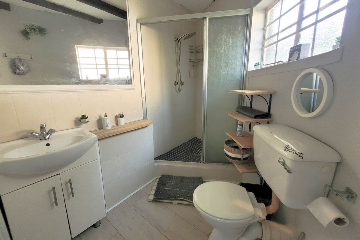 A functional bathroom featuring a vanity cabinet, shower enclosure, and toilet, with neutral finishes and natural light from a side window.