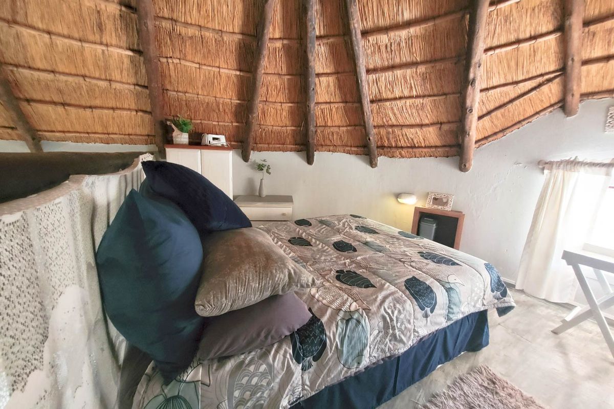 A bedroom featuring a unique exposed thatch roof with timber rafters and tiled flooring, offering a rustic aesthetic.