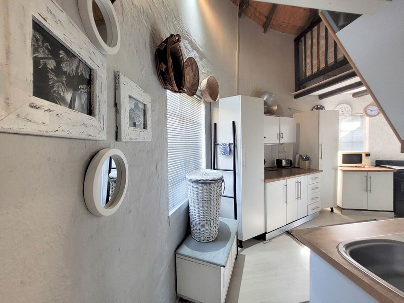 Compact kitchen featuring white cabinetry, laminate countertops, and a unique mezzanine level with exposed timber rafters, offering a rustic yet functional cooking space.