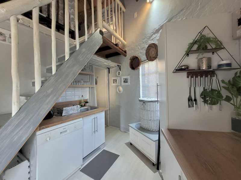 Compact kitchen area featuring built-in cabinetry, wooden countertops, a stainless steel sink, and an integrated dishwasher, situated beneath a timber staircase.