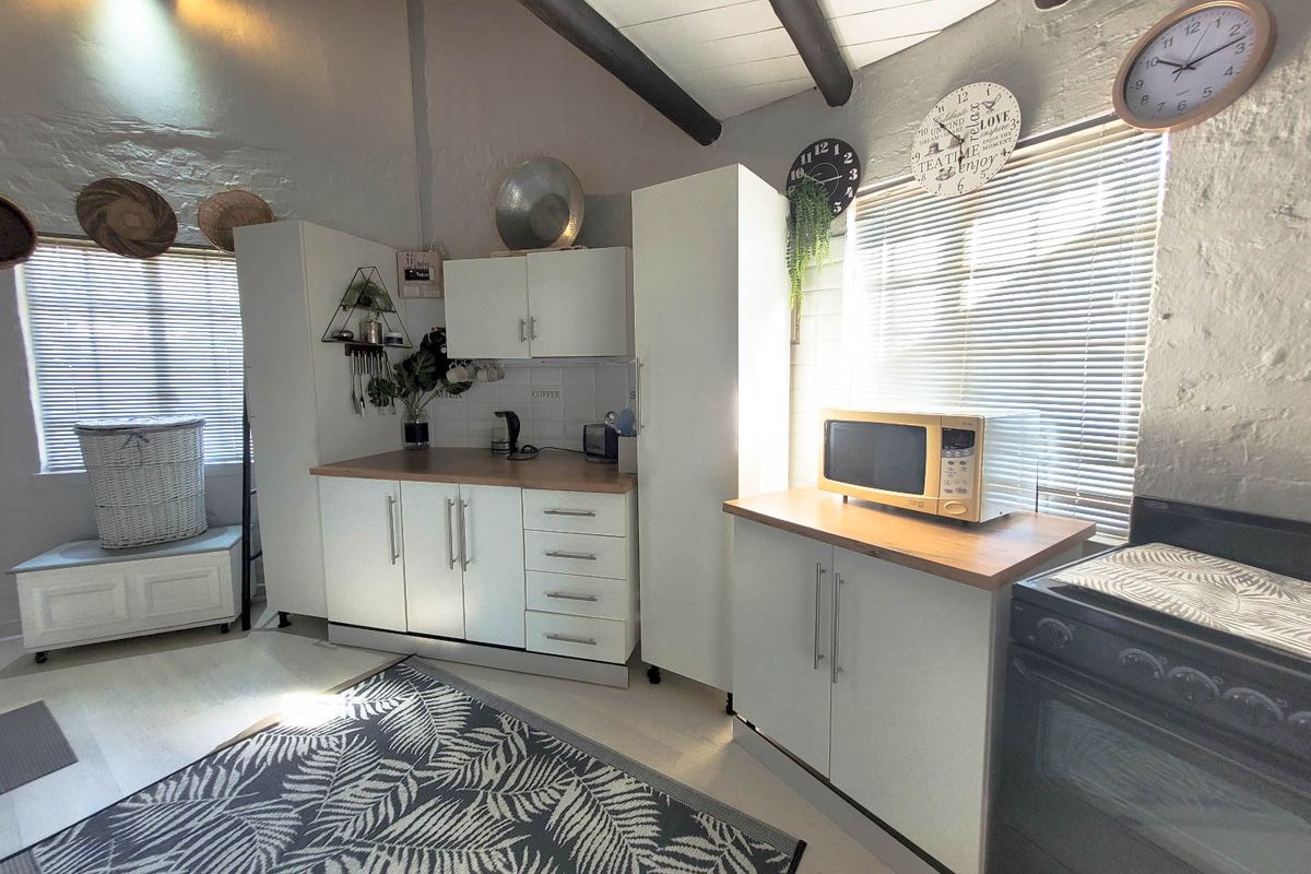 A compact kitchen featuring white cabinetry, timber-look countertops, tiled splashback, and exposed timber ceiling beams, providing a functional and bright workspace.
