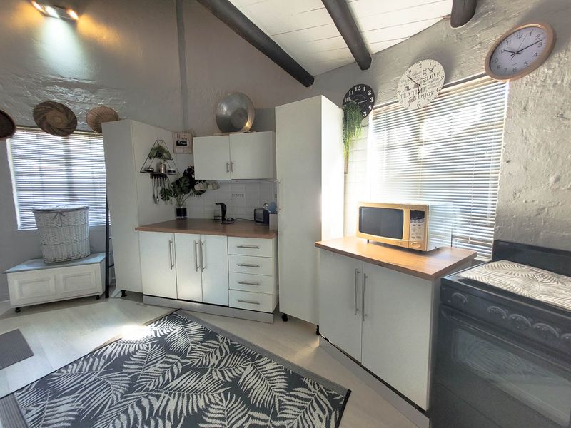 A compact kitchen featuring white cabinetry, timber-look countertops, tiled splashback, and exposed timber ceiling beams, providing a functional and bright workspace.