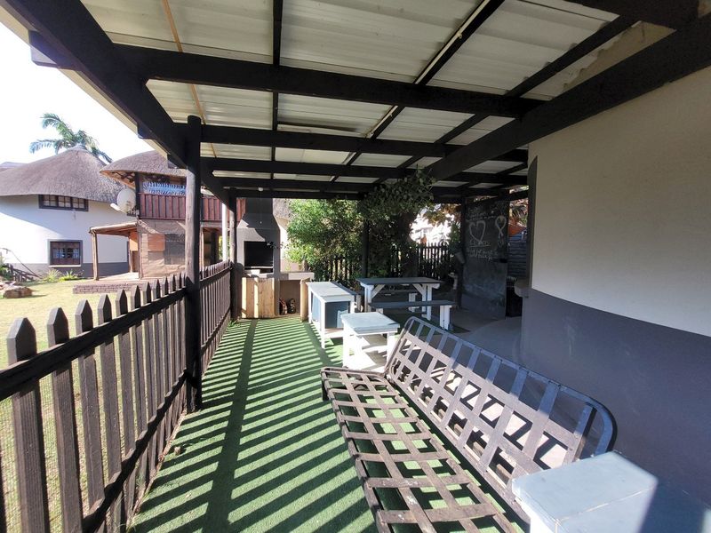 A covered outdoor patio area featuring a built-in braai, timber pergola structure, and fenced perimeter, ideal for outdoor entertaining.