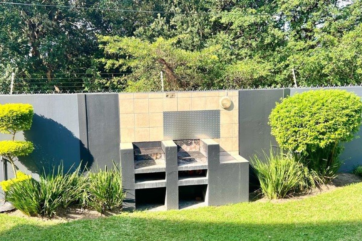 A well-maintained outdoor area featuring a built-in brick braai with a tiled splashback, set against a secure perimeter wall with electric fencing.
