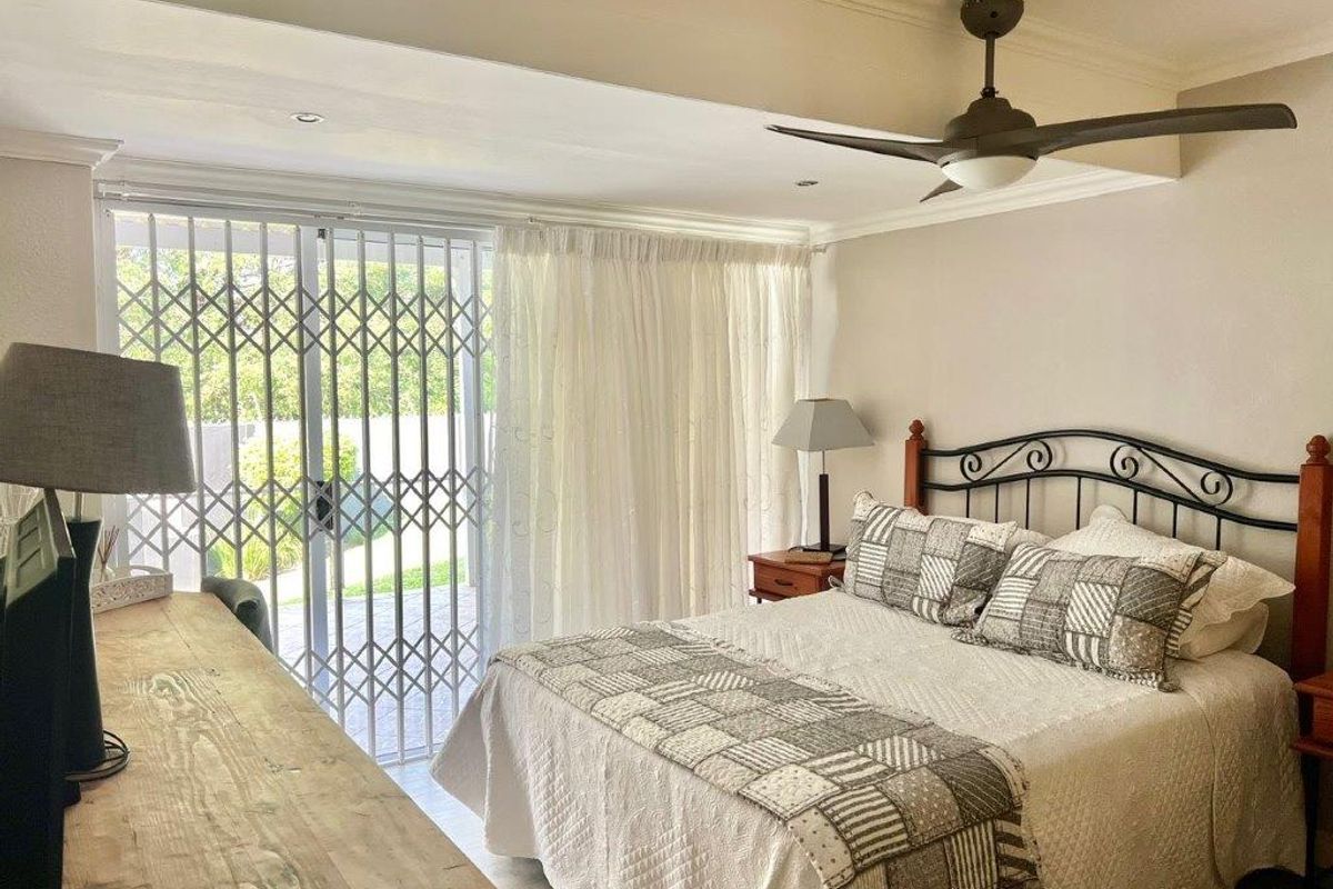 A well-lit bedroom featuring a ceiling fan, crown molding, and a sliding glass door with a security gate leading to an outdoor area.