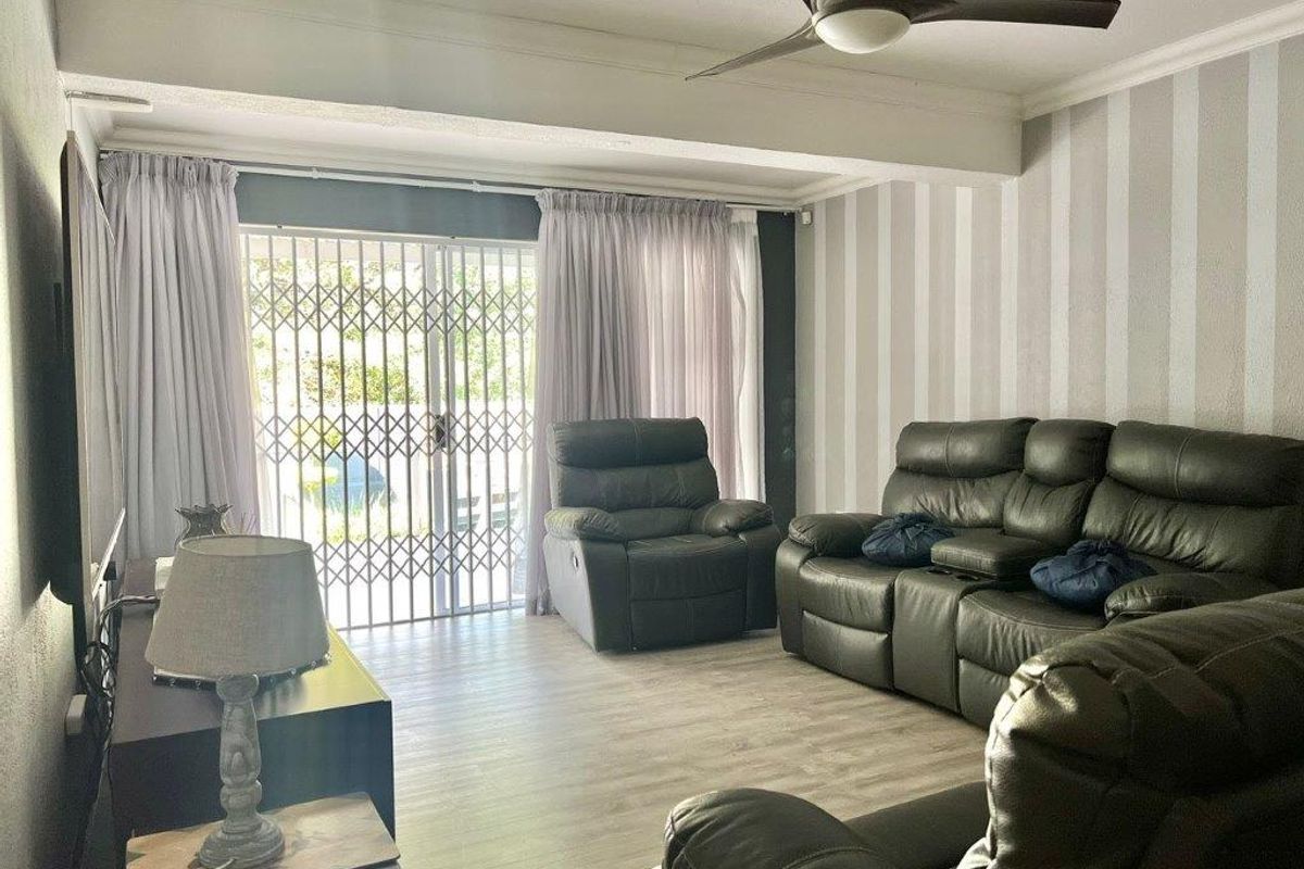 A living room featuring laminate flooring, a ceiling fan, and a sliding glass door with a security gate leading to the exterior.