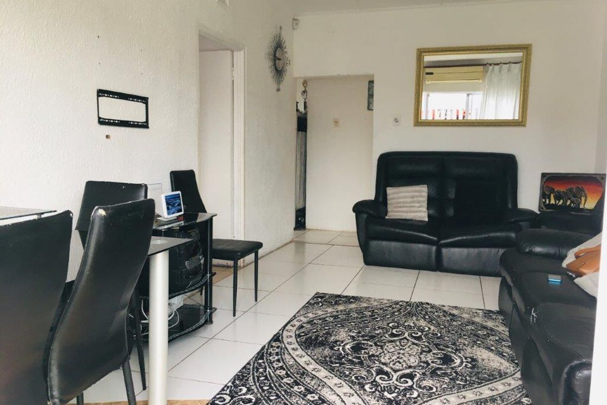 A living room area featuring white walls and ceramic floor tiles, showing signs of wear and requiring cosmetic updates.