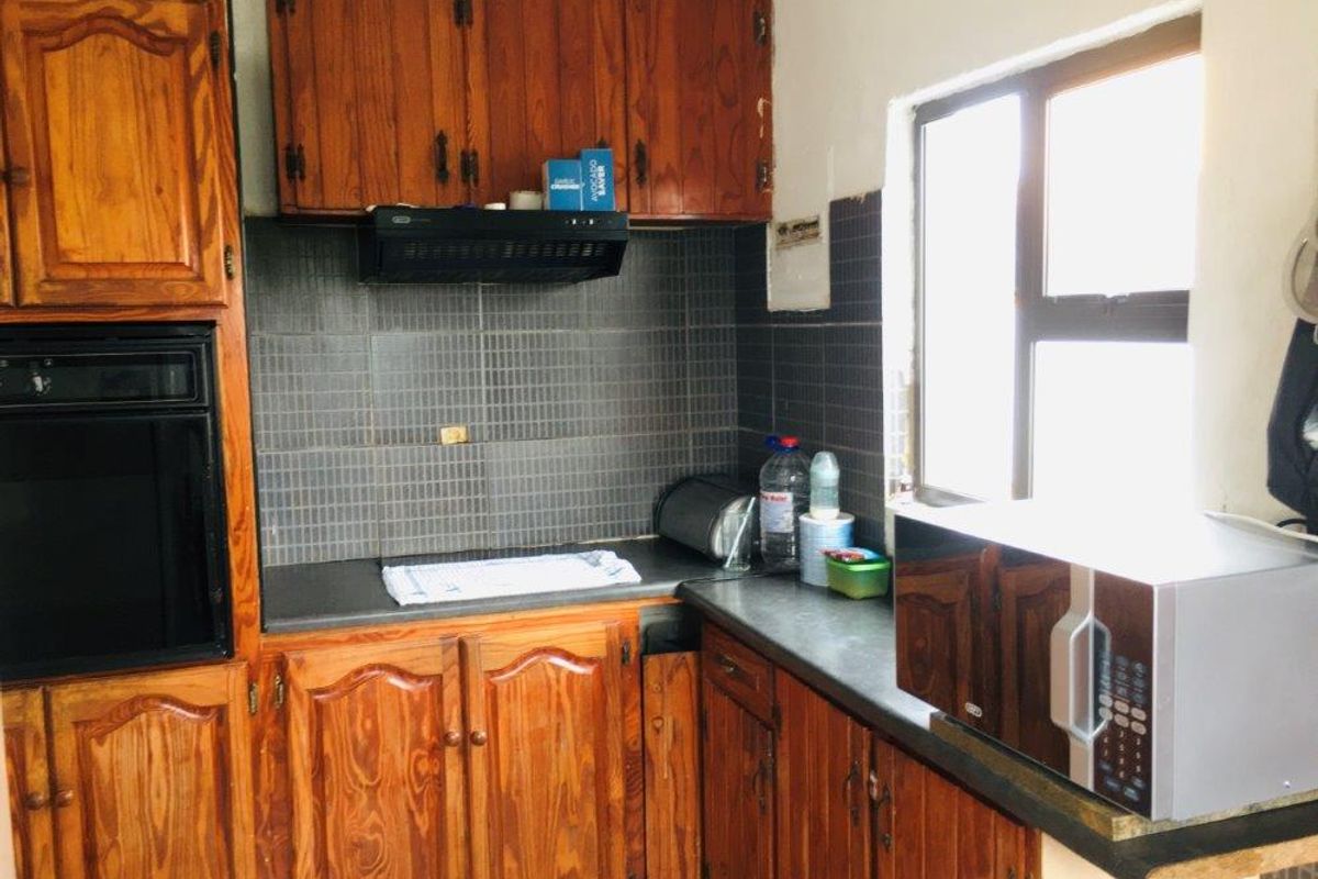 A dated kitchen featuring traditional wooden cabinetry, built-in oven, extractor fan, and dark tiled backsplash with ample counter space.
