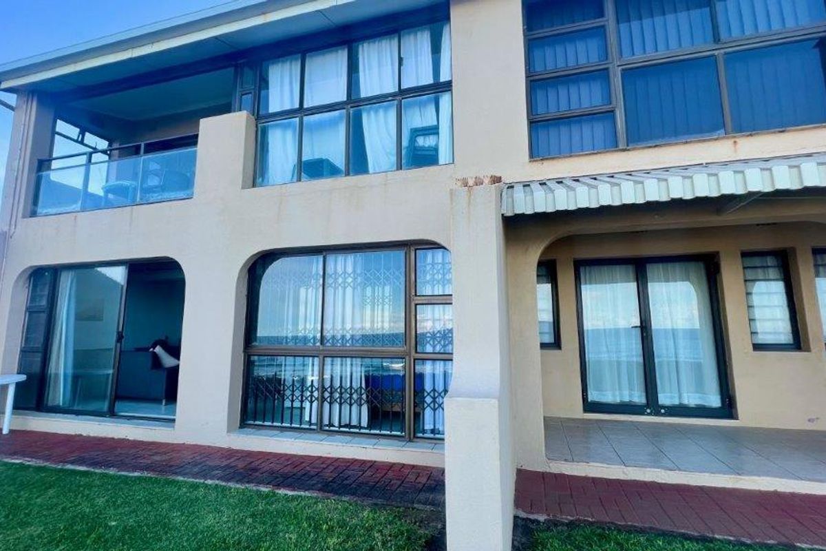 Rear elevation of a two-story apartment building featuring a ground-floor patio, upper-level balcony, and sliding glass doors with security gates.