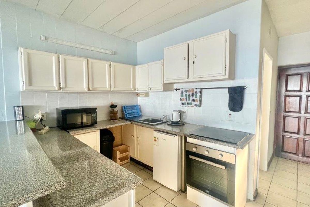A functional kitchen featuring granite countertops, built-in oven, electric hob, and ample cabinetry, finished with tiled flooring and a tiled backsplash.