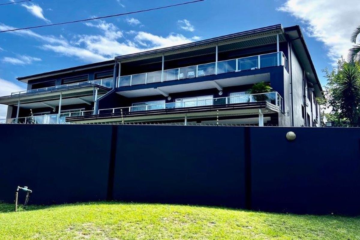 Rear view of a multi-story apartment building featuring tiered covered balconies with modern glass balustrades and a secure perimeter wall.