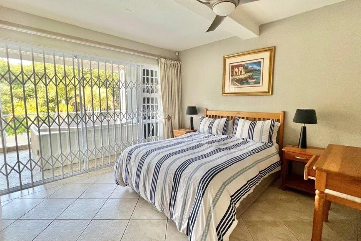 Spacious bedroom featuring tiled flooring, a ceiling fan, and large sliding glass doors with security gates leading to an outdoor area.