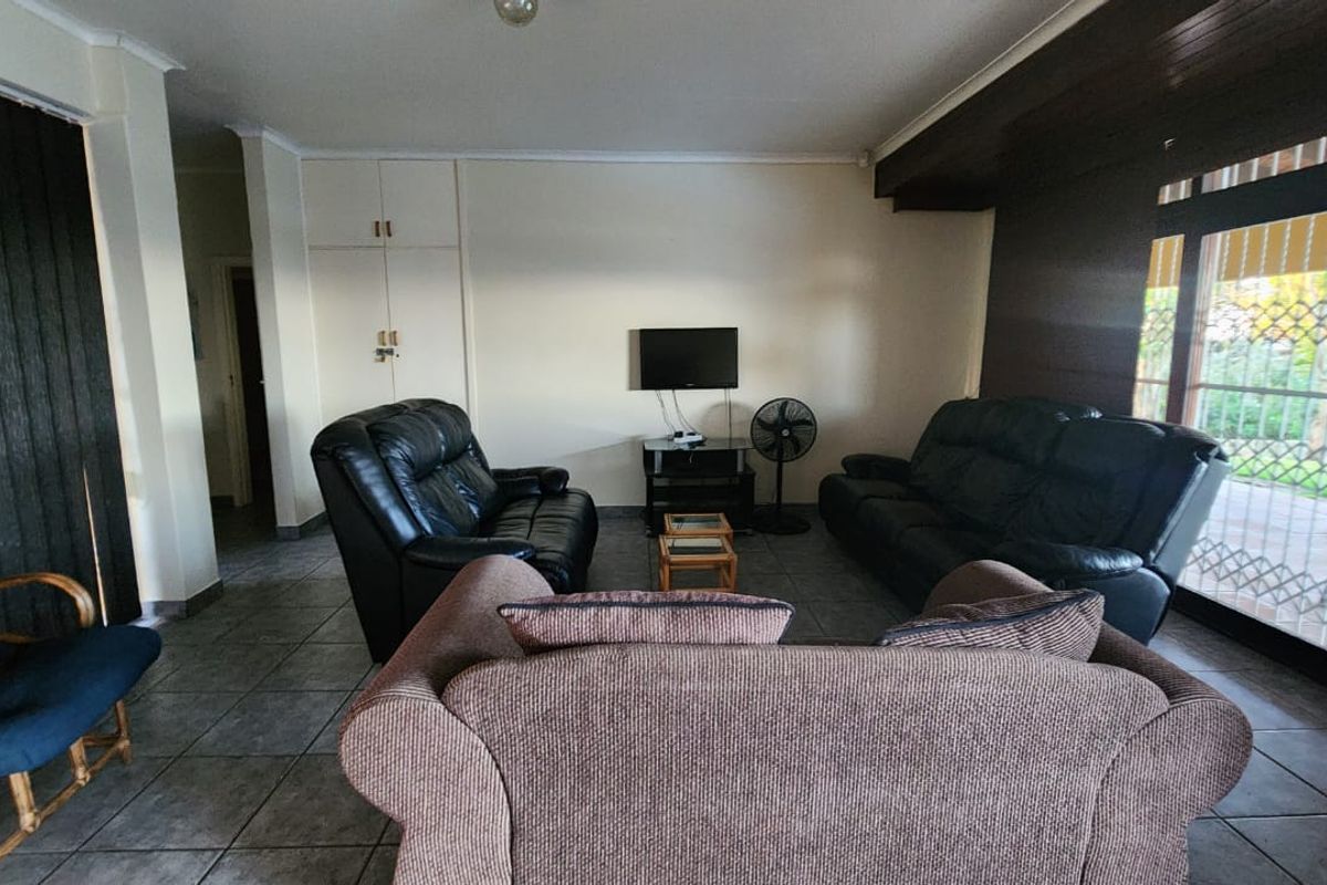 A spacious living room featuring tiled flooring, built-in storage cupboards, and a sliding glass door with security gate leading to the exterior.