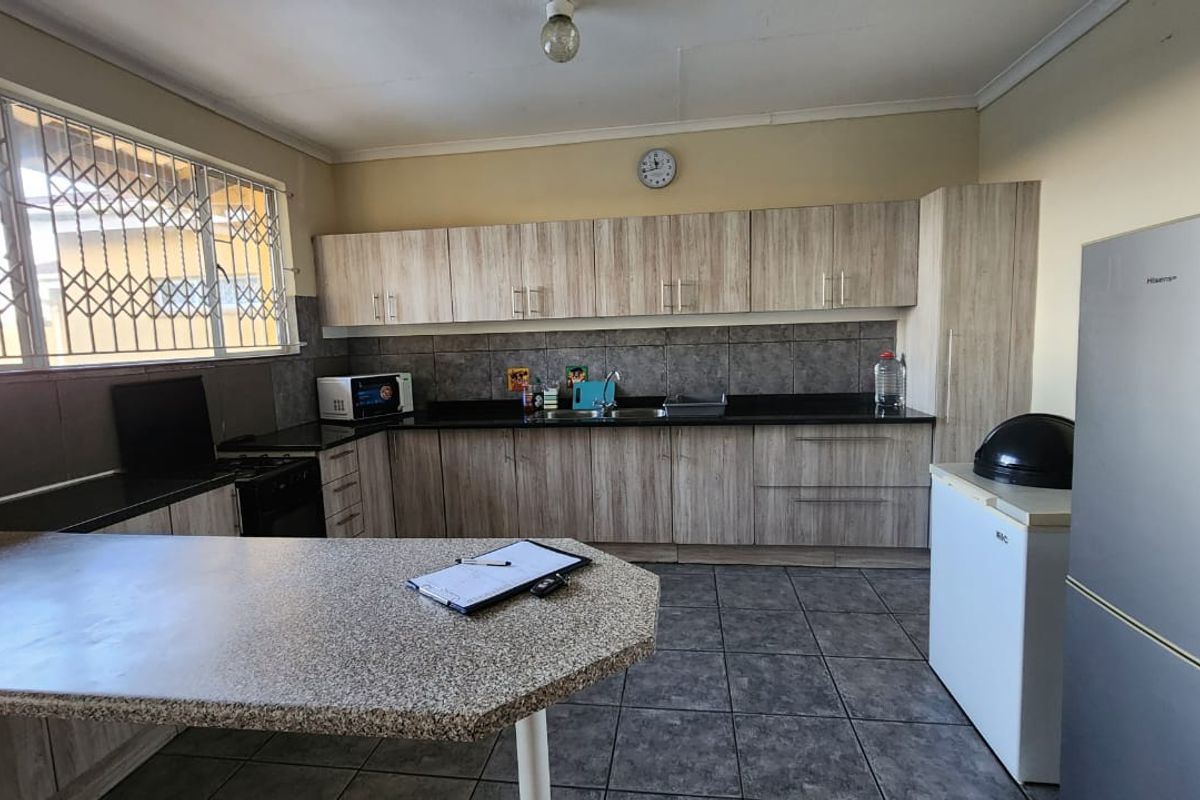 Functional kitchen featuring wood-look laminate cabinetry, granite countertops, a double basin sink, and tiled flooring with a breakfast nook area.