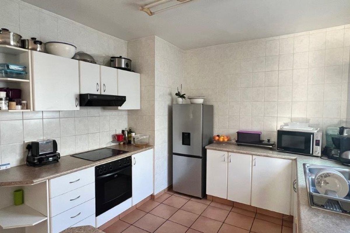 A functional kitchen featuring white cabinetry, laminate countertops, tiled backsplash, built-in oven, electric hob, and a stainless steel sink.