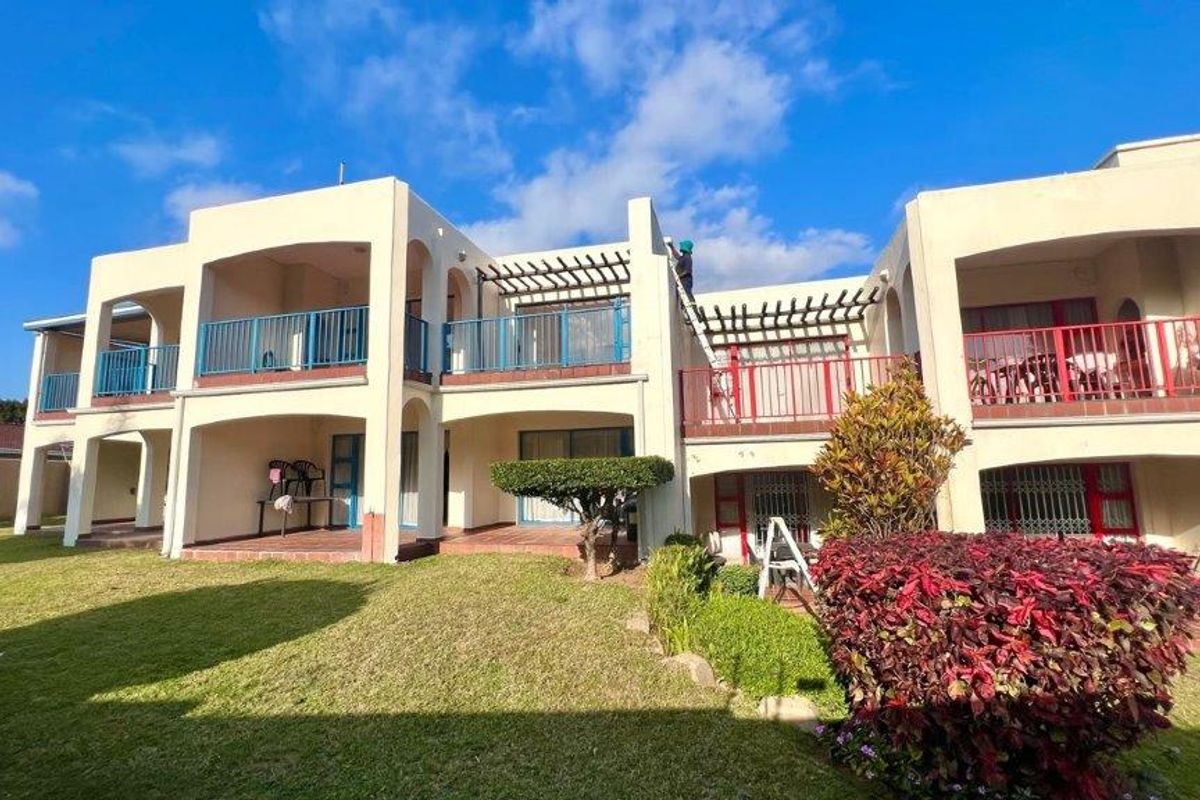Rear view of a multi-level apartment complex featuring private balconies, ground-floor patios, and a well-maintained communal garden area.