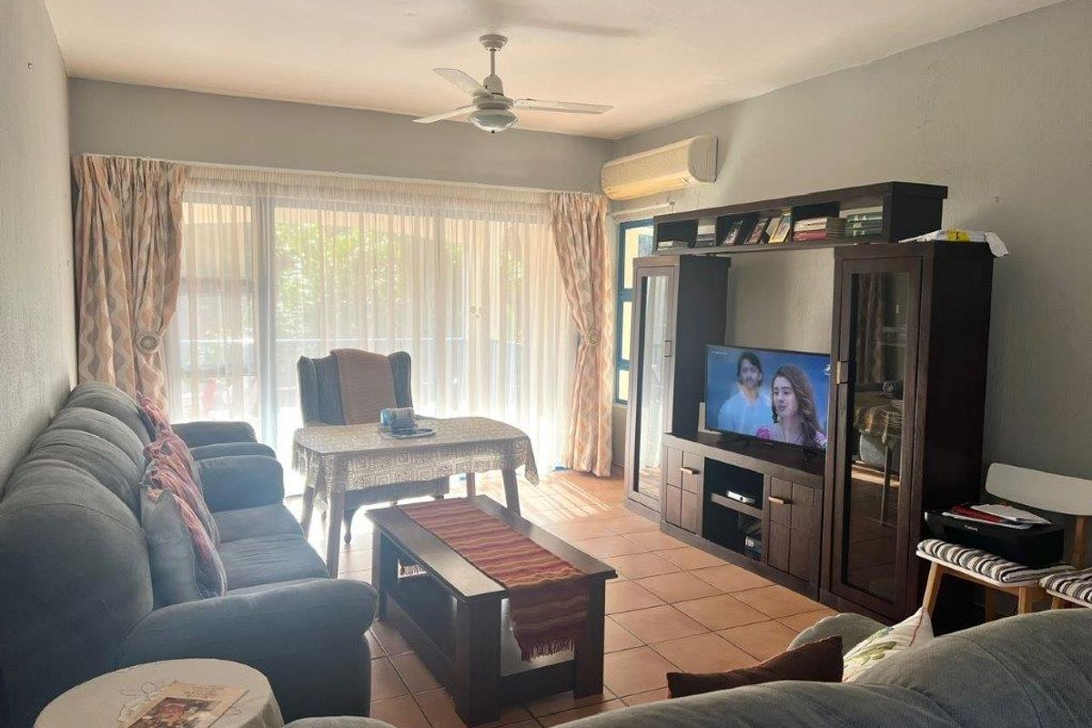 A comfortable living room featuring tiled flooring, a ceiling fan, and a split-system air conditioner, with large sliding doors providing access to the outdoors.